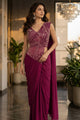 A woman models a sleeveless deep maroon saree with an intricately embroidered metallic bodice, set in a modern indoor hallway with marble floors and potted plants.