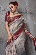 A woman models a traditional Indian saree with a silver-gray body, deep maroon borders, and gold zari patterns, set against a textured gray concrete wall. The brand name 'S-ethnic' and collection name 'RAKALLI' are visible in the top right corner.