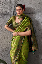 A woman models a green silk saree with gold zari embroidery and a matching blouse, standing against a textured gray concrete wall. The brand logo 'Sathvik Lifestyle' and collection name 'RAVALI 2600' are visible in the top right corner.