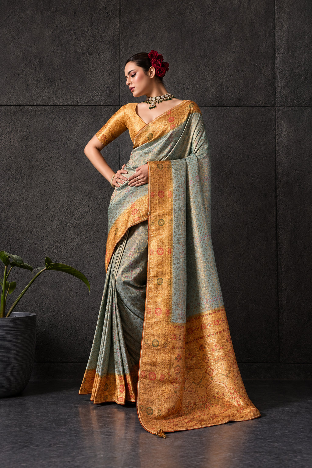 Woman wearing a traditional saree with a gray and gold design against a textured wall.