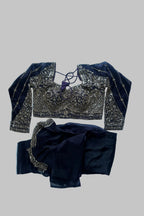 A dark navy blue traditional outfit laid flat on a white sheet, featuring an heavily embroidered blouse with gold and silver mirror work and a matching skirt.