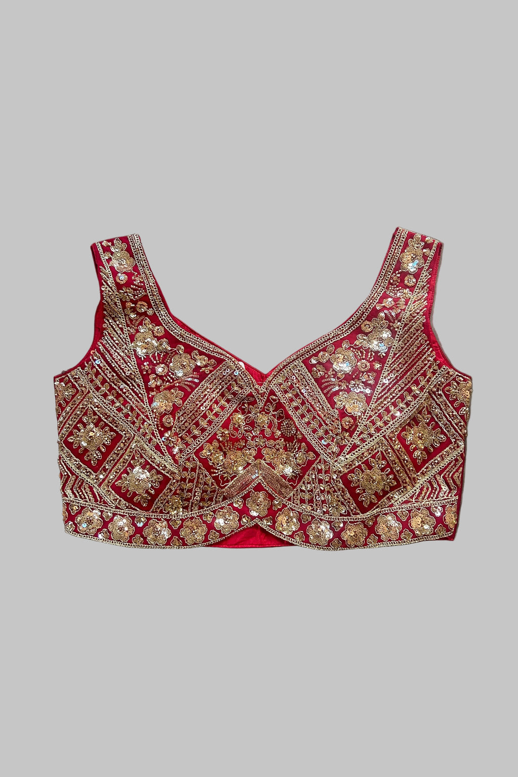A red and gold heavily embellished bridal blouse top with intricate mirror work and sequin embroidery, laid flat on a gray fabric background.