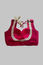 A bright pinkish-red sleeveless blouse top with a sweetheart neckline, decorated with a wide gold sequined border and red tie strings with gold tassels, laid flat on a gray fabric background.