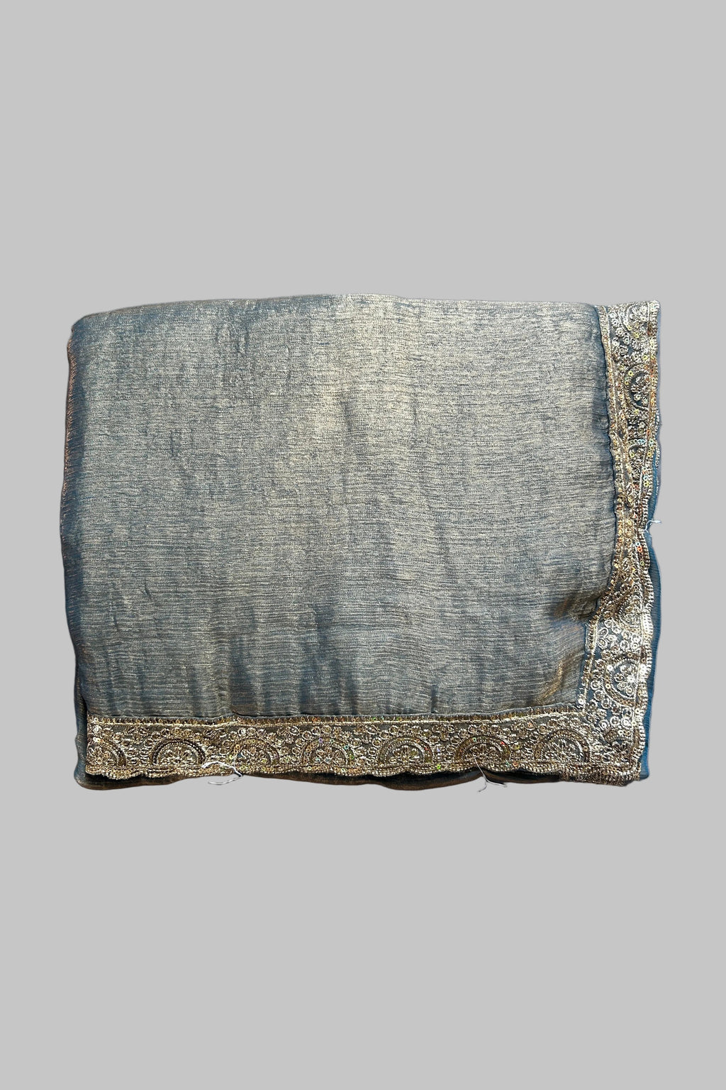 A folded piece of textured gray fabric with ornate gold embroidered borders, laid flat on a wrinkled gray fabric background.