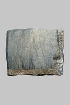 A folded piece of textured gray fabric with ornate gold embroidered borders, laid flat on a wrinkled gray fabric background.