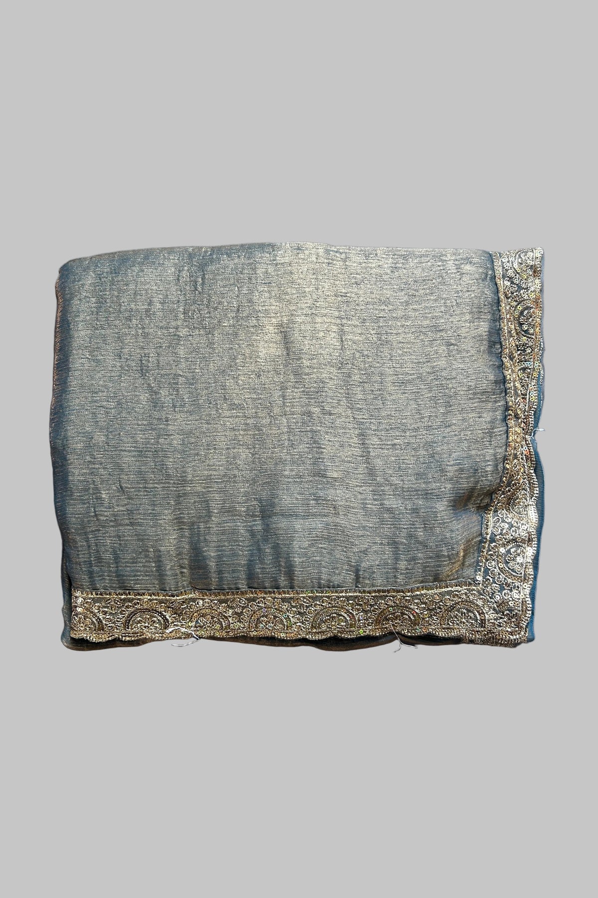 A folded piece of textured gray fabric with ornate gold embroidered borders, laid flat on a wrinkled gray fabric background.