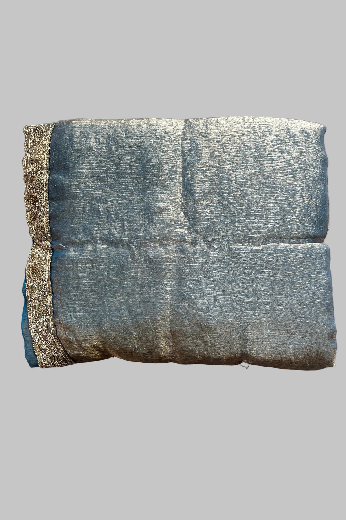 A folded piece of textured blue-gray fabric with a decorative metallic gold border, laid flat on a gray fabric background.