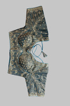 An embroidered blouse top laid flat on a gray fabric background, featuring a dark teal-green base with intricate gold zari embroidery and metallic embellishments.