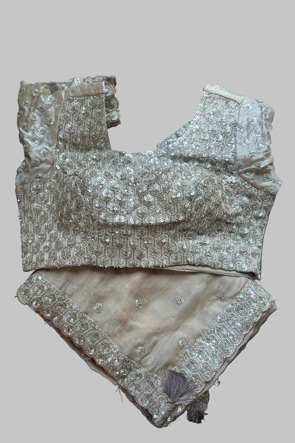 A beige and silver embellished traditional Indian outfit consisting of a heavily decorated sleeveless blouse and matching embroidered shorts, laid flat on a dark gray fabric background.
