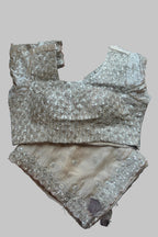A beige and silver embellished traditional Indian outfit consisting of a heavily decorated sleeveless blouse and matching embroidered shorts, laid flat on a dark gray fabric background.