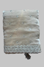 A folded beige fabric piece with silver embroidered floral motifs and a decorative embroidered border, placed on a dark gray fabric background.