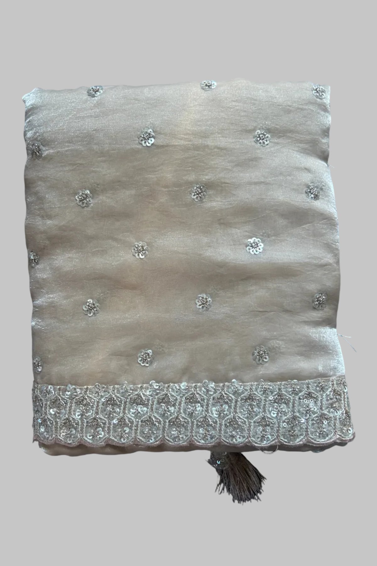 A folded beige fabric piece with silver embroidered floral motifs and a decorative embroidered border, placed on a dark gray fabric background.