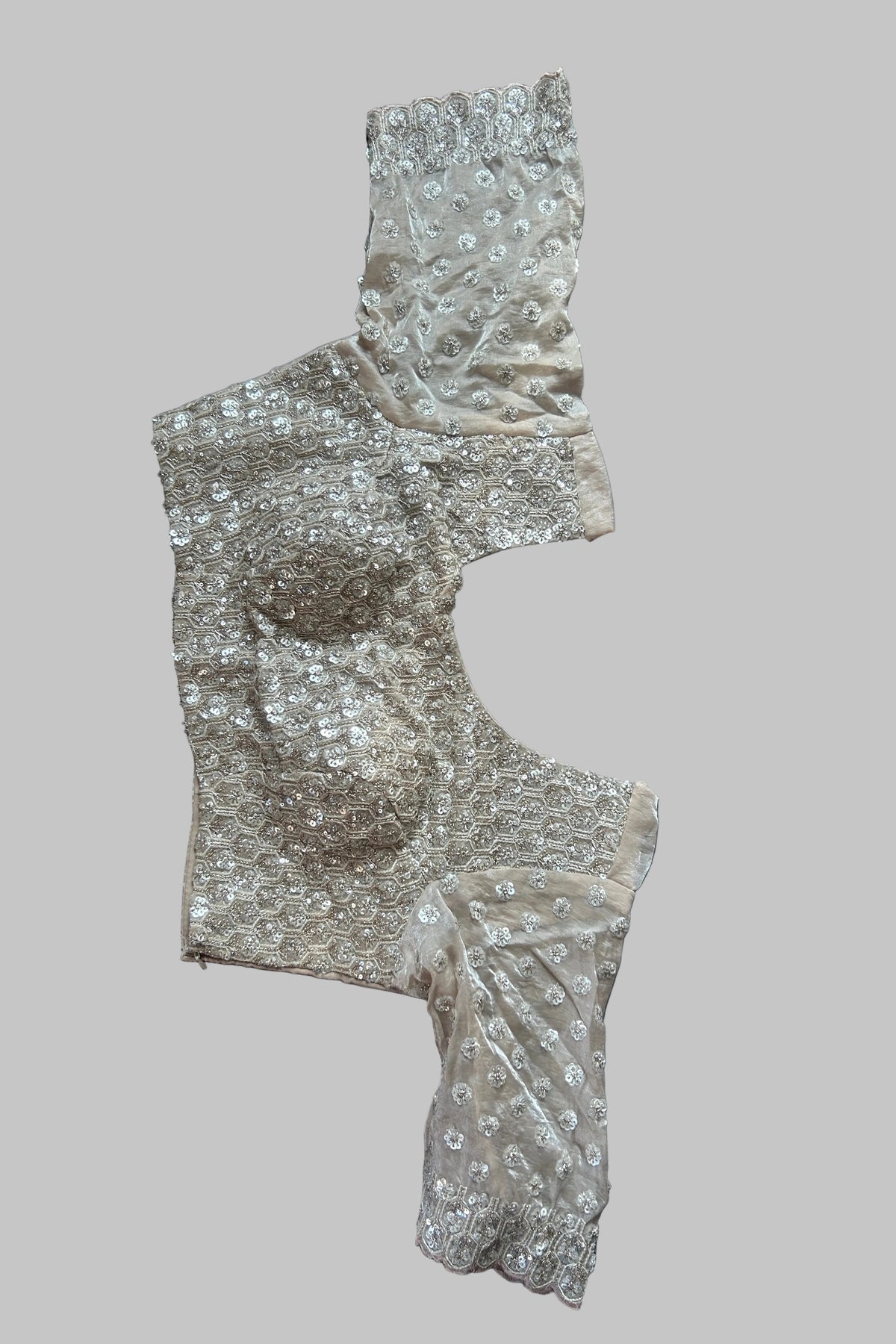 A beige and silver embellished lace garment laid flat on a dark gray fabric background.
