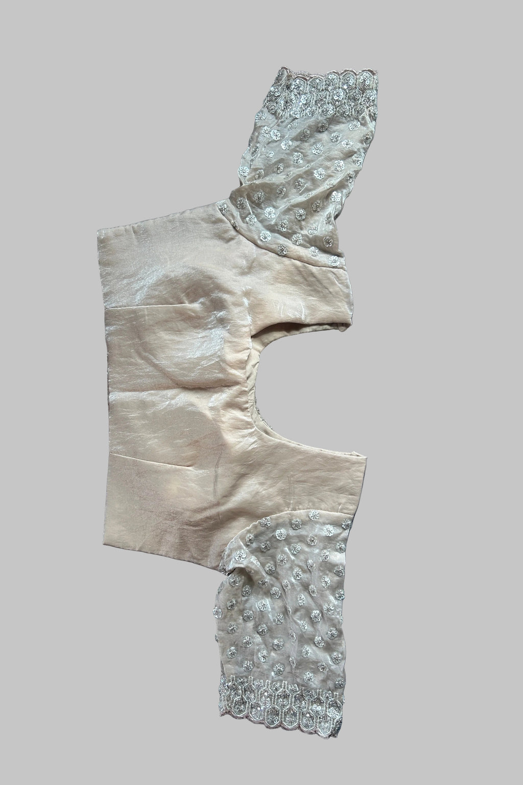 A vintage beige satin garment piece with intricate silver beadwork and lace trim, laid flat on a gray fabric background.