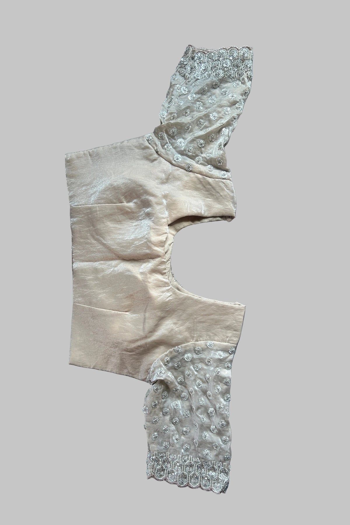 A vintage beige satin garment piece with intricate silver beadwork and lace trim, laid flat on a gray fabric background.