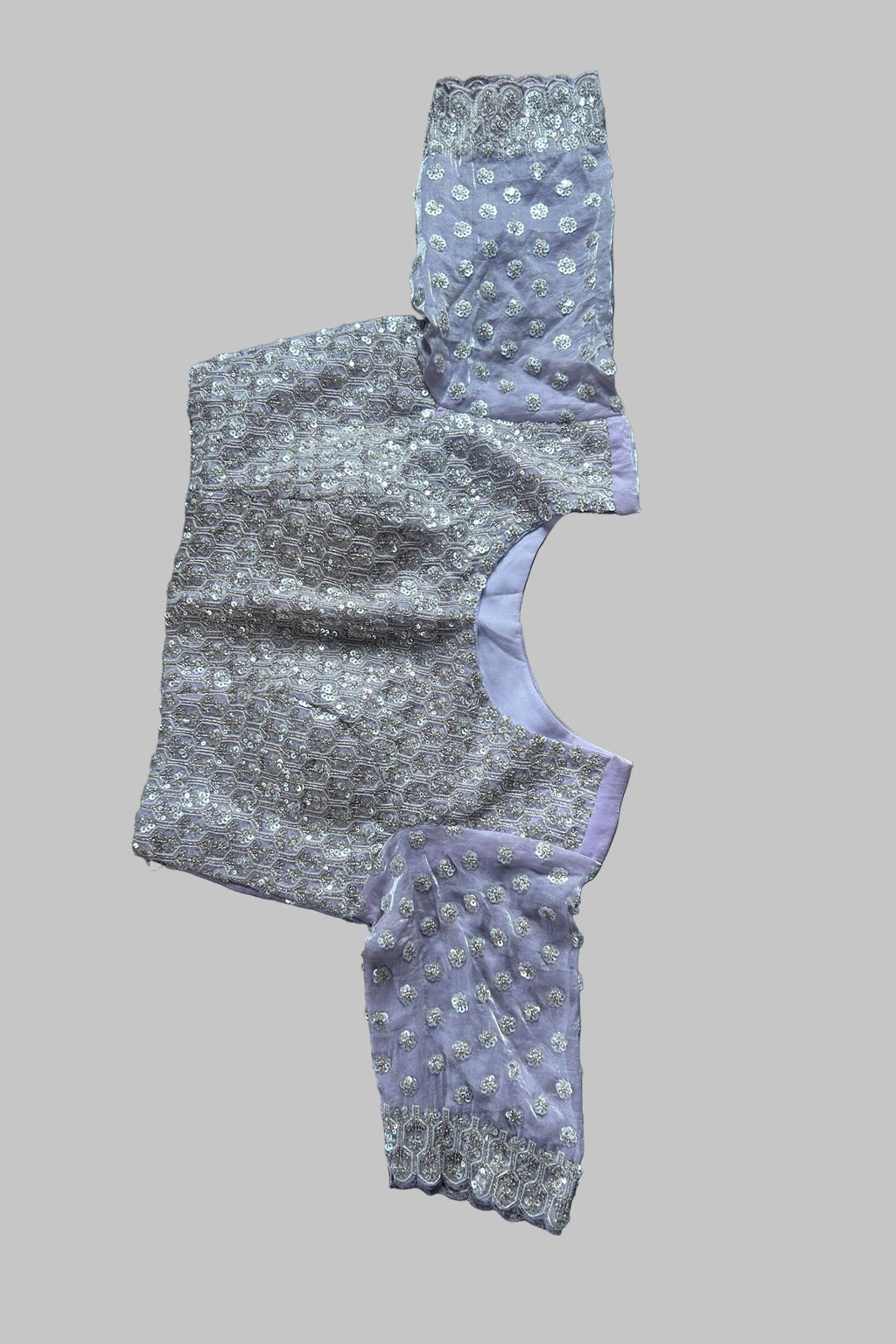 A lavender and silver embellished garment laid flat on a dark gray fabric background.