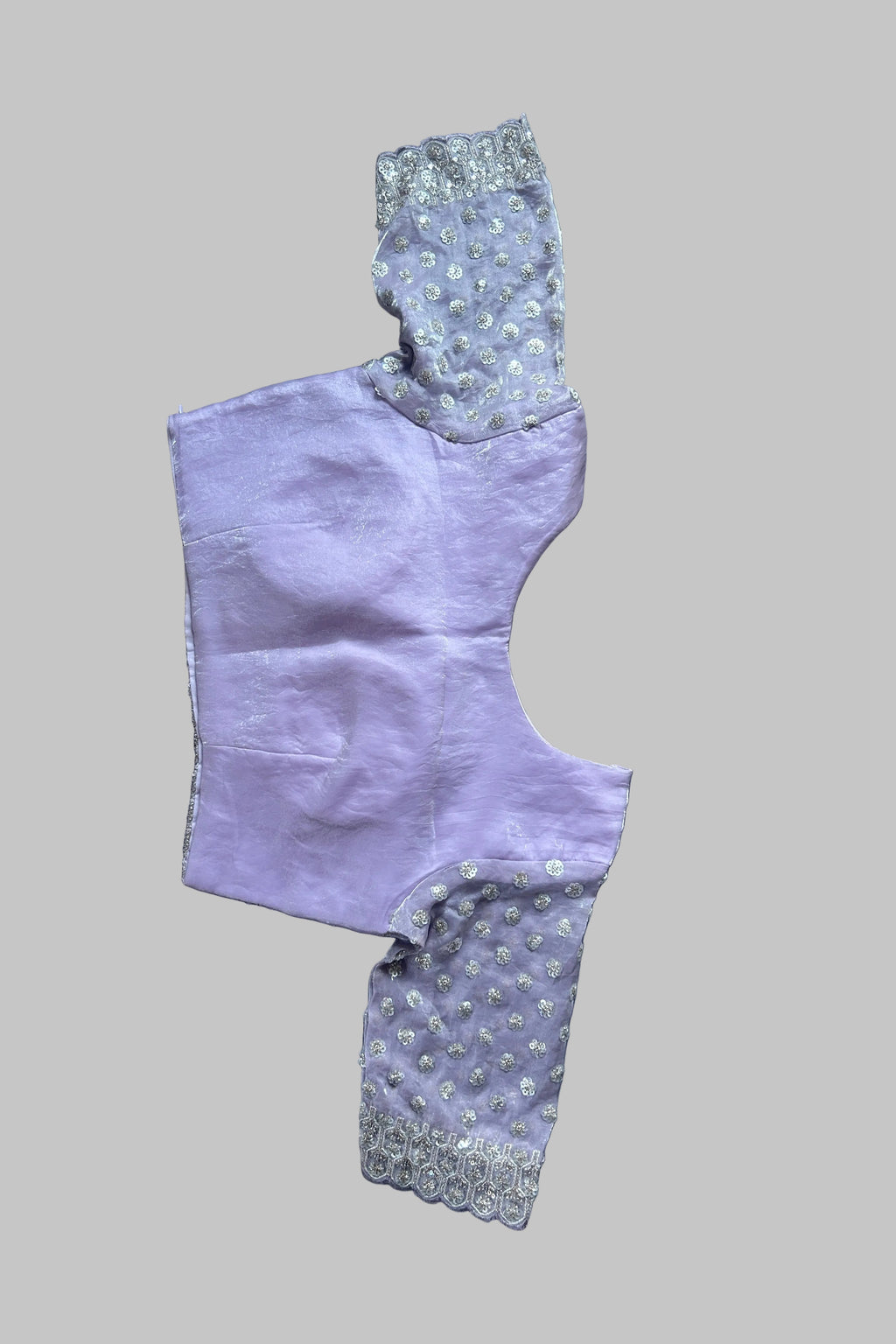 A lavender purple garment laid flat on a gray fabric background, featuring light gray and white patterned sleeves with lace trim.