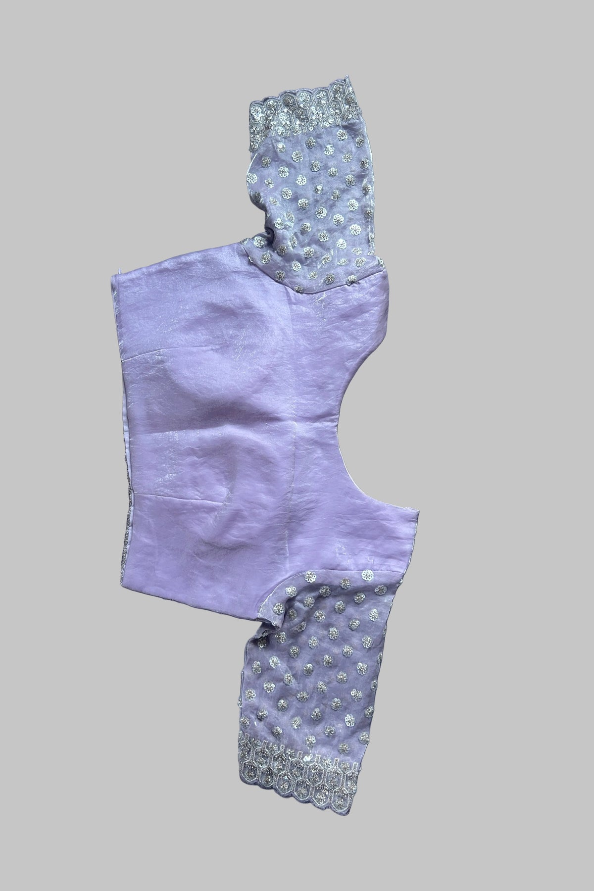 A lavender purple garment laid flat on a gray fabric background, featuring light gray and white patterned sleeves with lace trim.