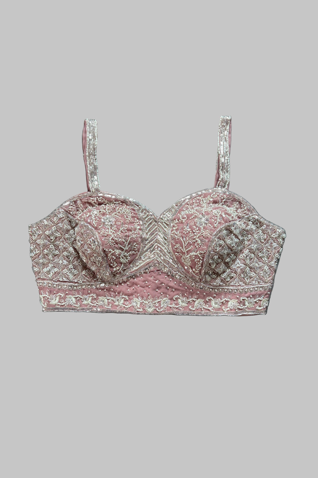 A pink and silver embroidered bralette with thin straps, laid flat on a gray fabric background.