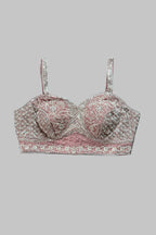 A pink and silver embroidered bralette with thin straps, laid flat on a gray fabric background.