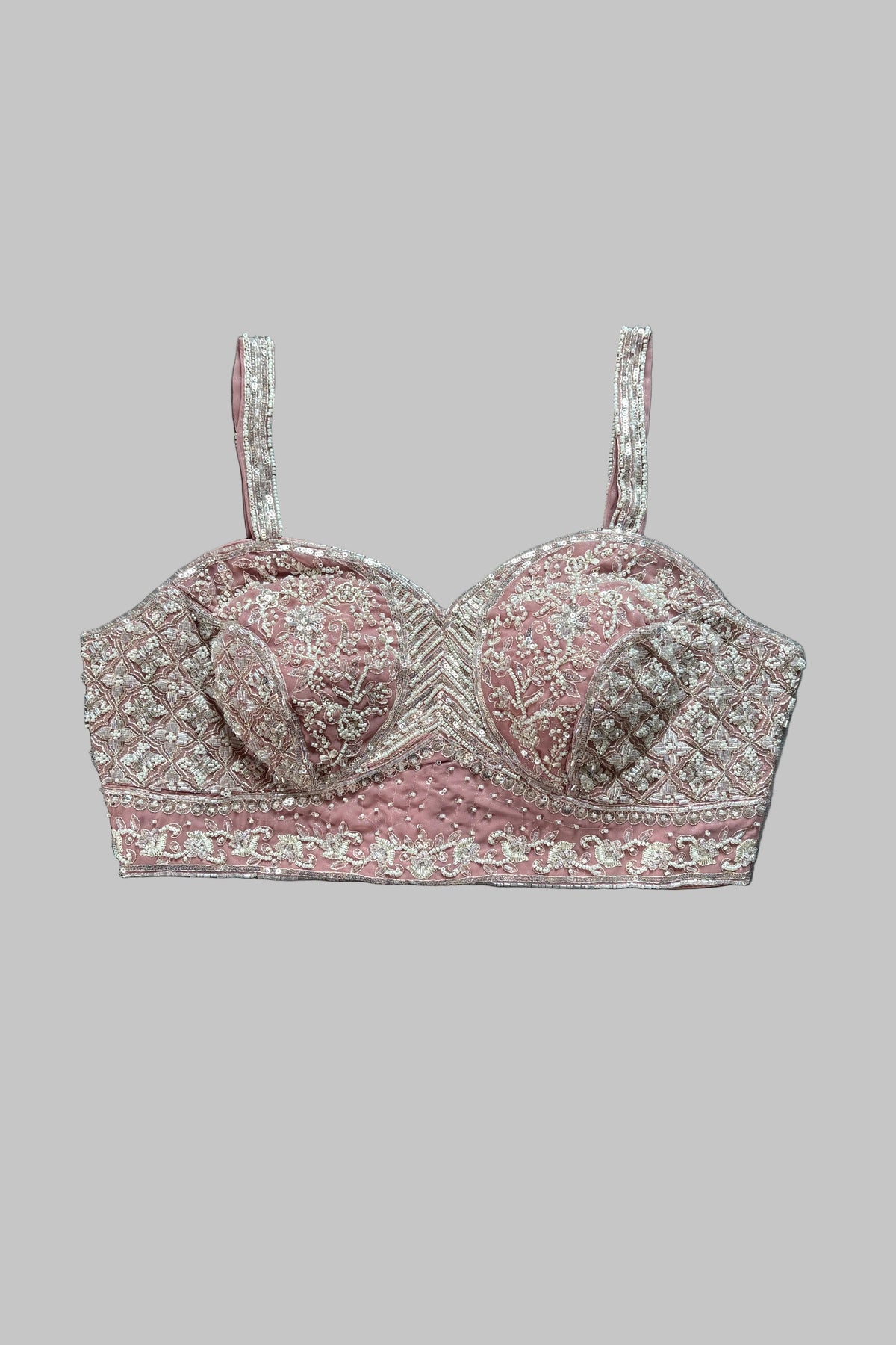 A pink and silver embroidered bralette with thin straps, laid flat on a gray fabric background.