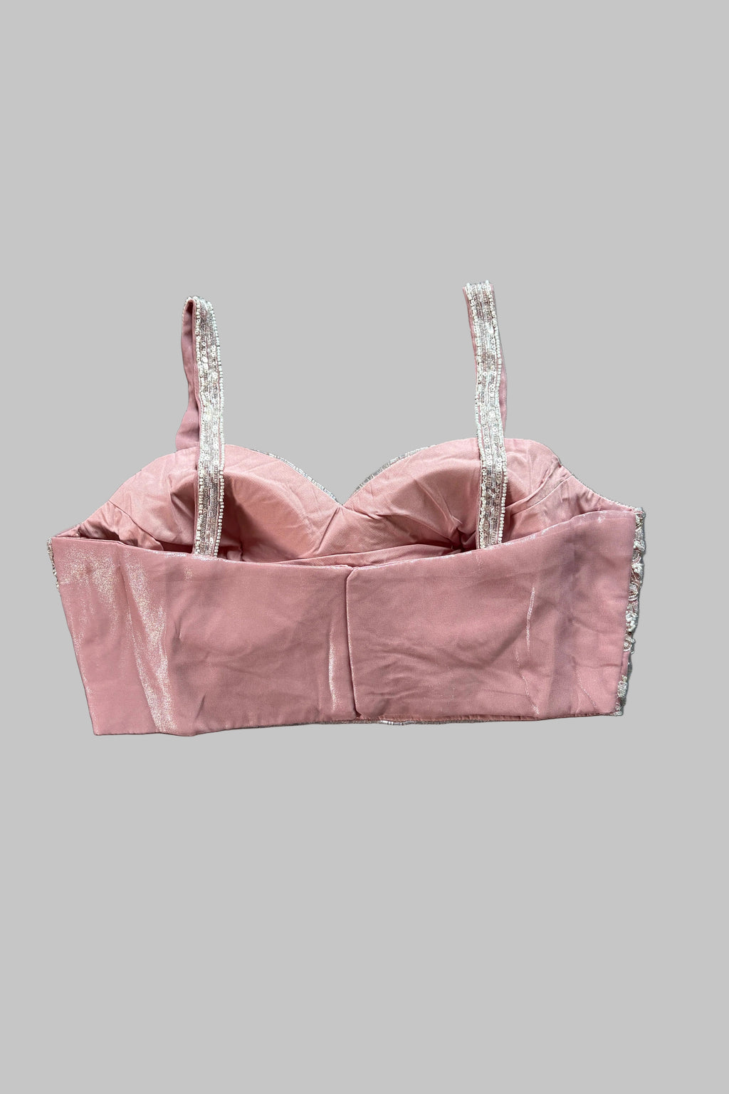 A dusty pink velvet bustier crop top with silver rhinestone-embellished straps, laid flat on a wrinkled gray fabric background.