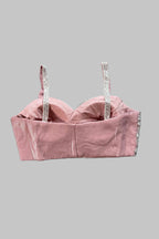 A dusty pink velvet bustier crop top with silver rhinestone-embellished straps, laid flat on a wrinkled gray fabric background.