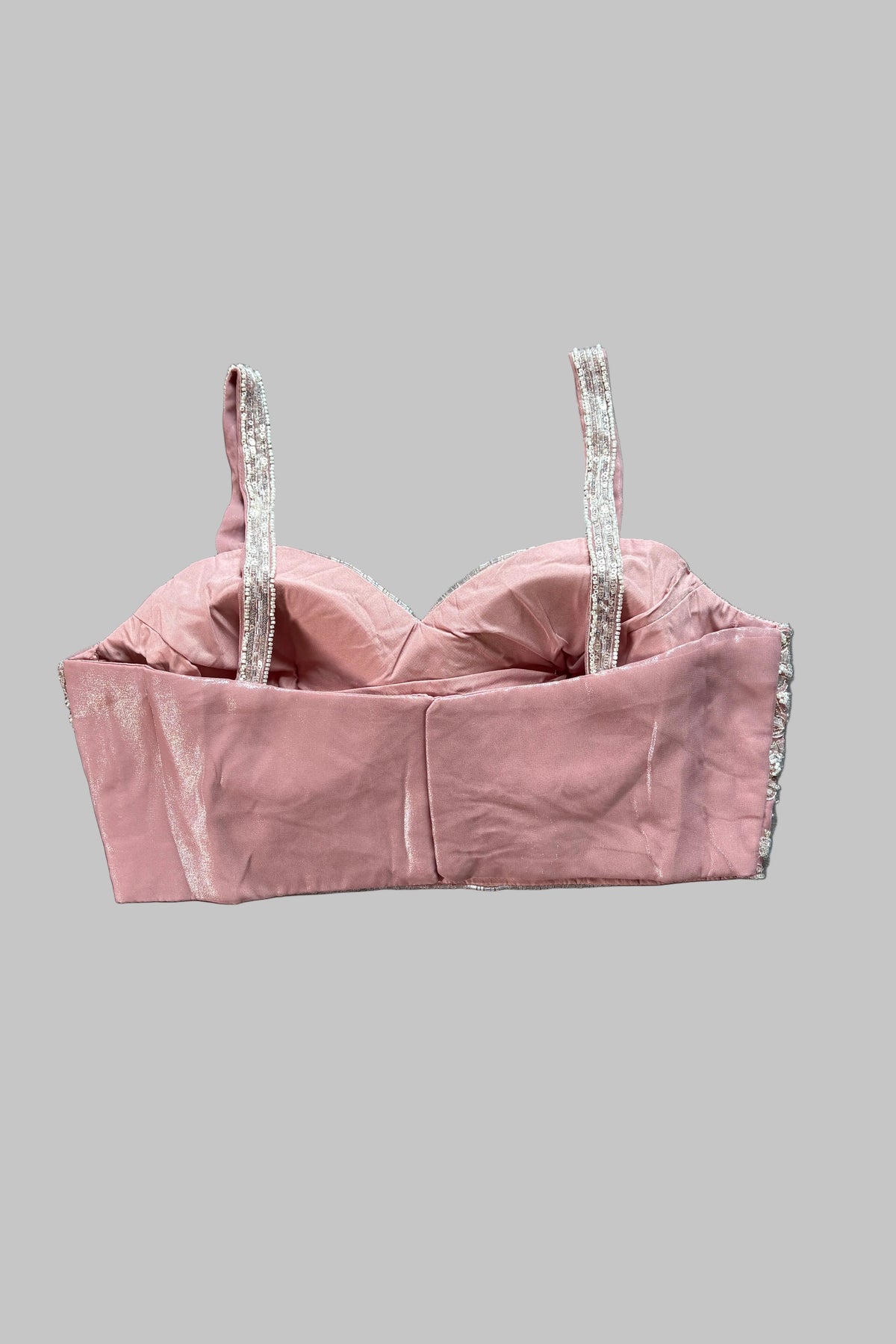 A dusty pink velvet bustier crop top with silver rhinestone-embellished straps, laid flat on a wrinkled gray fabric background.