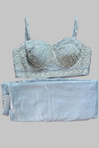 A light blue lace and embroidered bralette laid flat on a gray fabric surface, with matching folded light blue pants or a skirt placed underneath it.