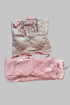 A folded two-piece clothing set laid flat on a gray bedsheet. The set includes a light pink and white patterned top with a bow at the neckline and matching light pink pants.