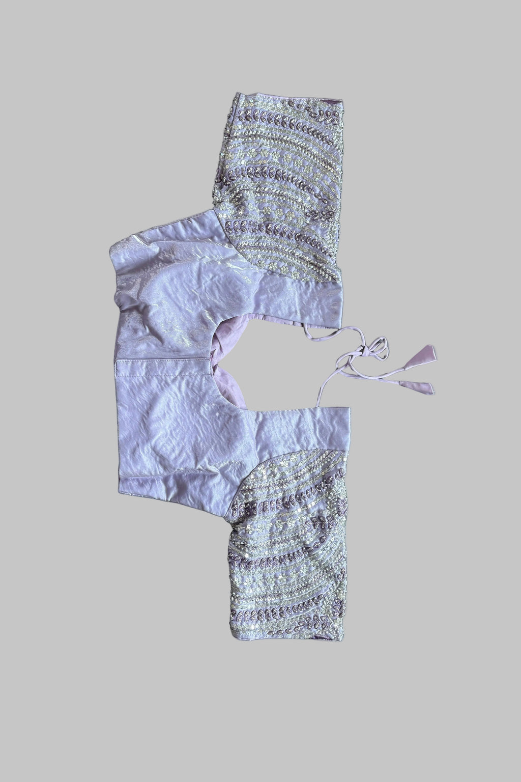 A lavender and patterned cropped tunic top laid flat on a gray bed, with bare feet visible in the corners.