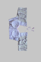 A lavender and patterned cropped tunic top laid flat on a gray bed, with bare feet visible in the corners.