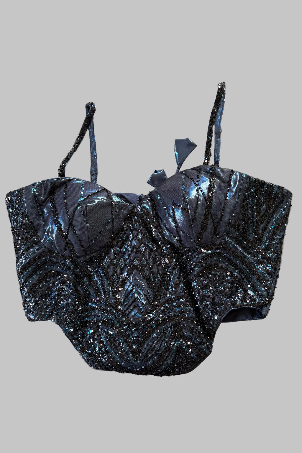 A dark blue sequined corset-style top with matching bottoms laid flat on a wrinkled light gray sheet.