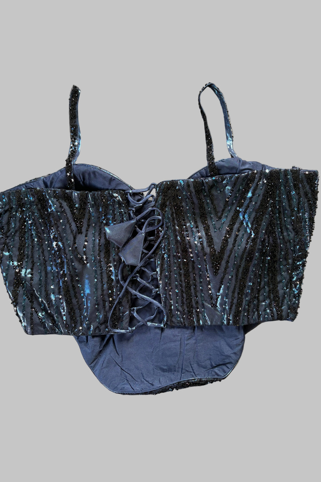 A dark blue sequined lace-up bustier top with thin shoulder straps, laid flat on a wrinkled light gray fabric background.