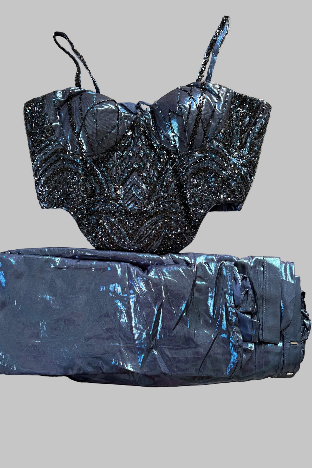 A two-piece outfit consisting of a black and blue beaded corset-style top and matching shiny blue pants, laid flat on a light gray fabric surface.