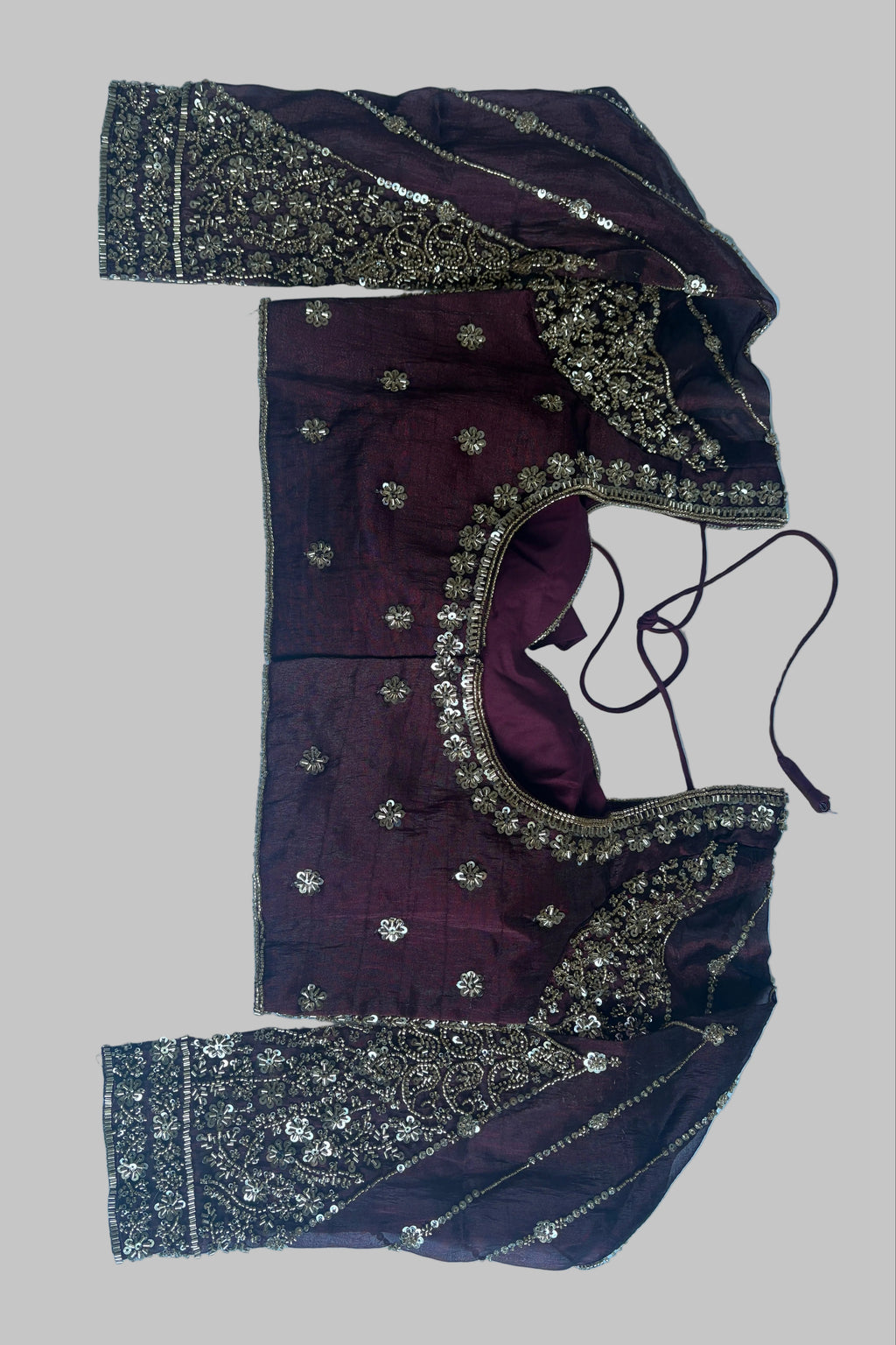 A dark plum purple embroidered blouse top with gold and silver mirror work and sequin borders, laid flat on a light blue fabric background.