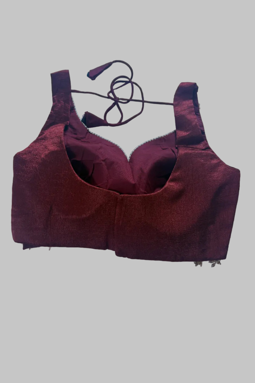 A dark red or burgundy bralette with wide shoulder straps and a matching neck strap, laid flat on a wrinkled light blue fabric background.