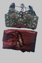A traditional Indian ethnic wear set consisting of a heavily embroidered maroon and gold blouse with a matching tie-neck cord and folded maroon skirt with a coordinating embroidered border, laid flat on a white sheet.