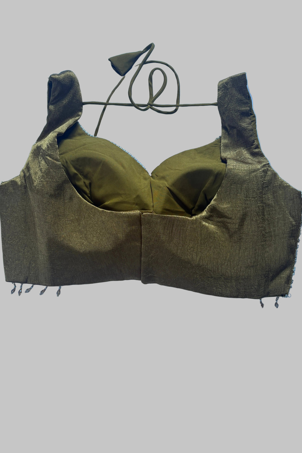 An olive green fabric bralette or underwire bra laid flat on a light blue wrinkled sheet. The garment has a textured shimmering fabric, a center seam, and a thin matching cord tie at the top.