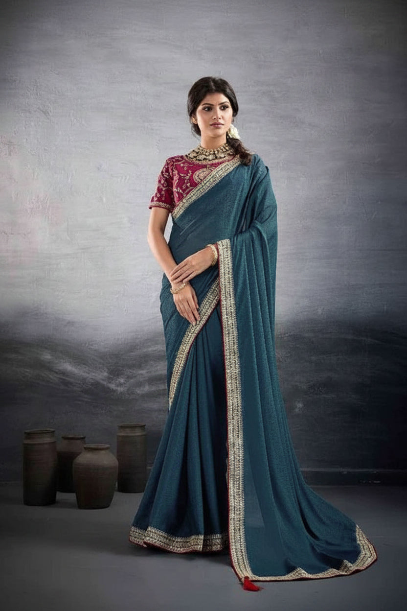 A woman models a teal blue saree with a red and gold embroidered blouse against a textured gray studio backdrop. The brand name 'suma MEHAR' is visible in the top right corner.