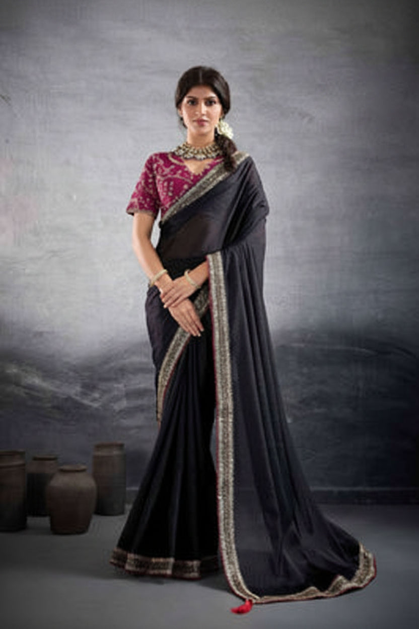A woman modeling a traditional Indian saree in a studio setting, shown in two side-by-side views. The saree is black with a metallic gold border, paired with a rich magenta pink embroidered blouse.