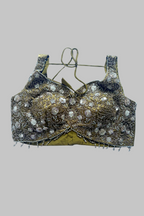 An ornate gold and black embellished blouse top with intricate beadwork, sequins, and silver-toned decorative details, shown against a solid gray background.