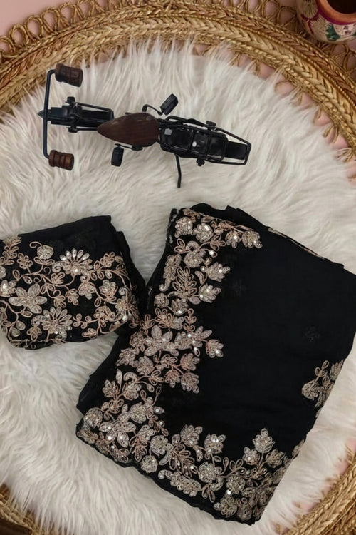 Black georgette saree fabric set with beige floral embroidery, shown folded with a matching black blouse piece and a large draped dupatta on a white background, alongside a decorative motorcycle prop.