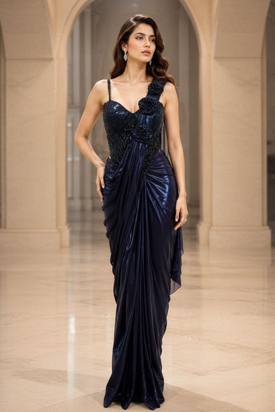 Two women modeling floor-length evening gowns in an arched indoor hallway. The left gown is dark navy blue with a ruched bodice and sheer draped skirt.