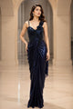 Two women modeling floor-length evening gowns in an arched indoor hallway. The left gown is dark navy blue with a ruched bodice and sheer draped skirt.