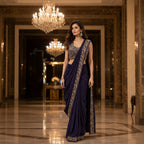 Woman in a dark blue saree with gold embroidery in an elegant indoor setting.