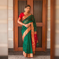 Woman wearing a green saree with a red blouse standing in front of a wooden door.