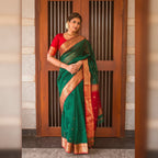 Woman wearing a green saree with a red blouse standing in front of a wooden door.