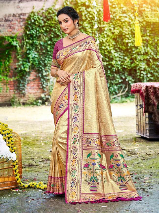 Woman wearing a traditional beige saree with colorful patterns in an outdoor setting.