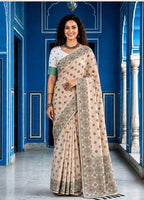 Woman wearing a beige saree with a pattern in front of a blue wall.